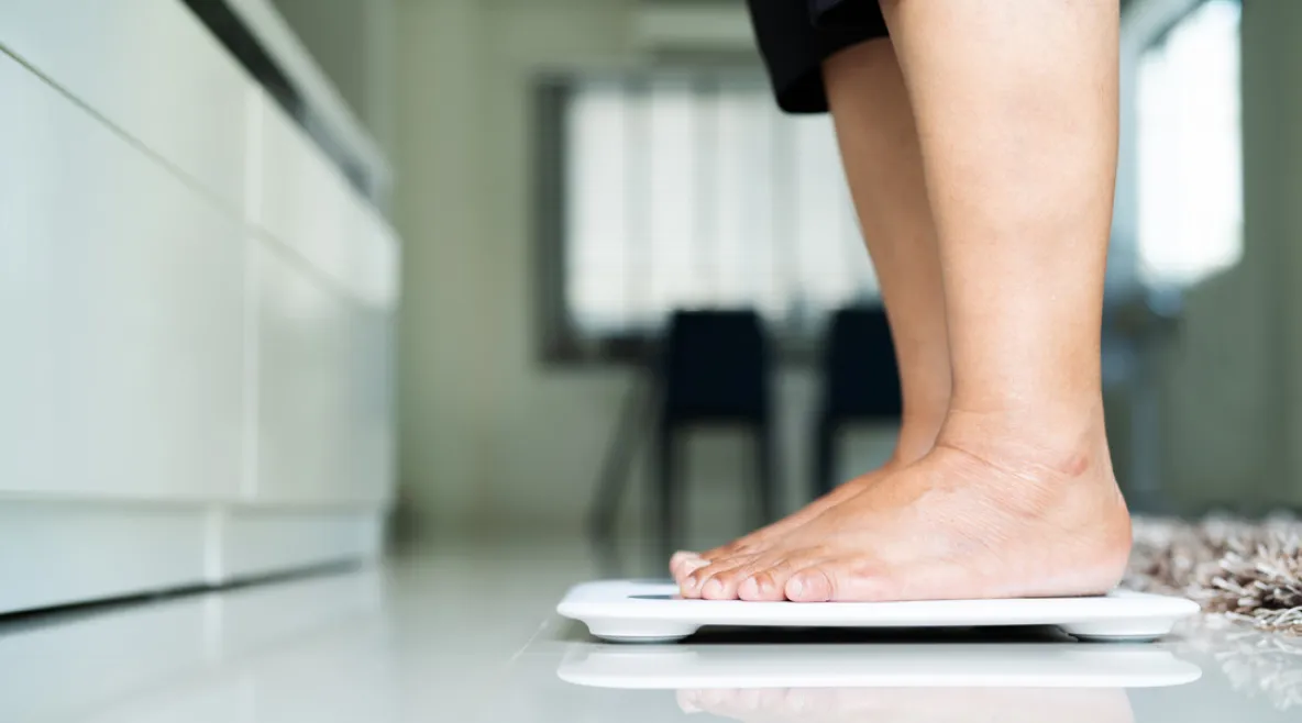 Henkilö seisoo keittiössä vaa'an päällä punniten itsensä. Tutkimus: Painon kehityksen seuranta voi auttaa tunnistamaan tyypin 2 diabeteksen riskipotilaita.