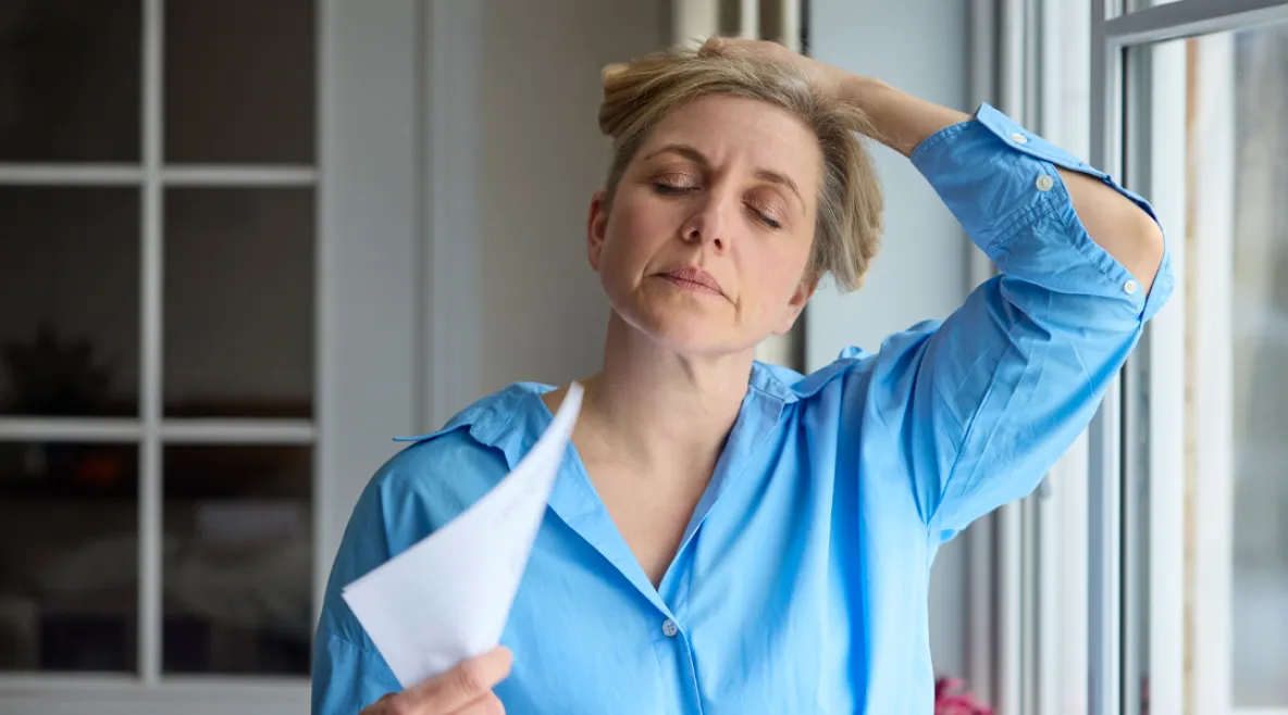 Kuumista aalloista kärsivä nainen tuulettaa paperinipulla kasvojaan.