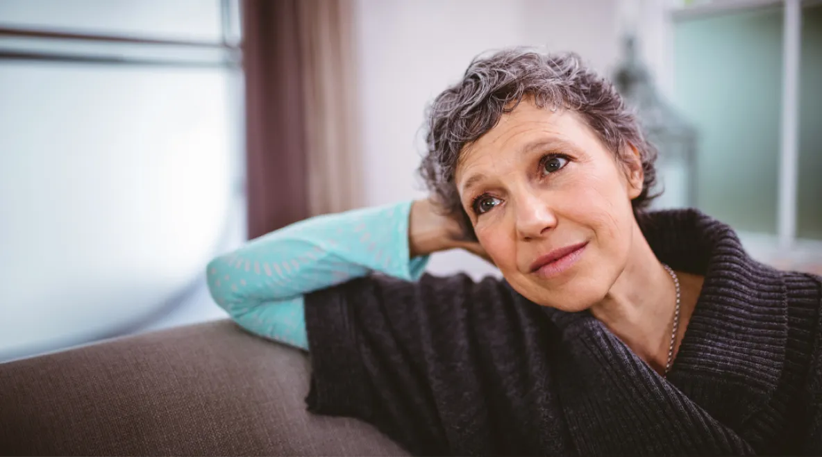 Hieman hiuksista harmaantunut nainen nojaa käteensä ja katsoo ikkunasta ulos.