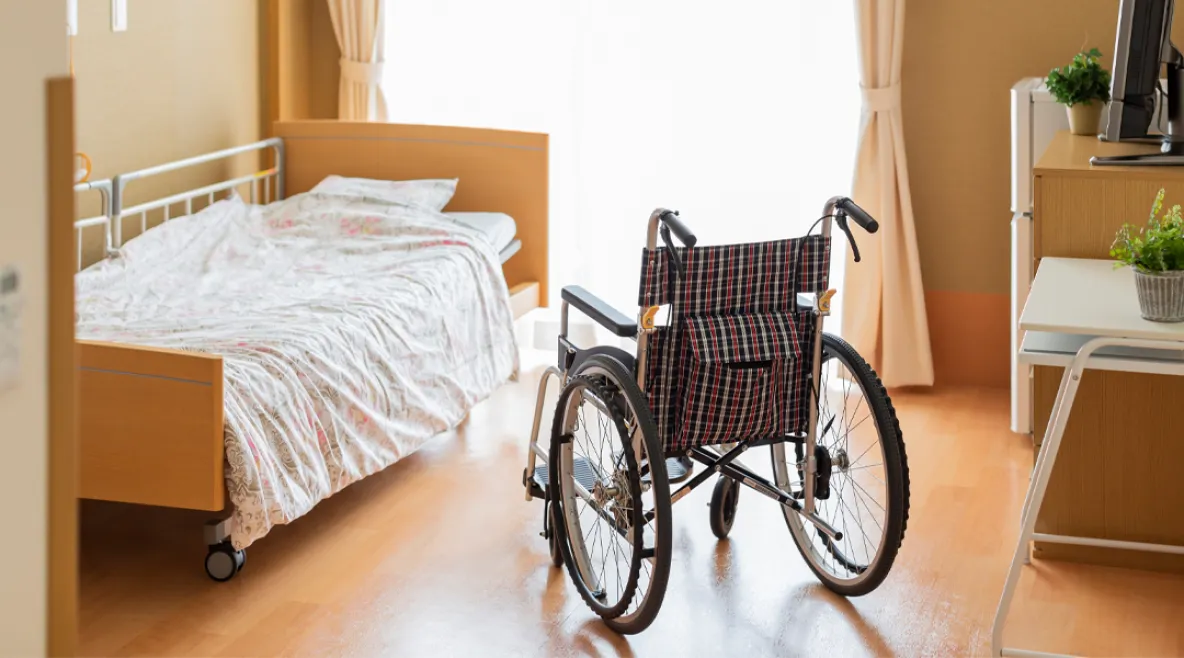 Asukkaan huone vanhainkodissa. Sänky ja pyörätuoli ikkunan ääressä.