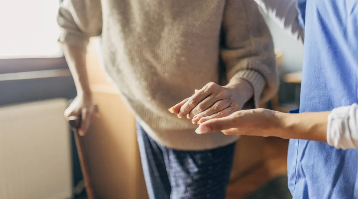 Hoitaja ohjaa kävelykeppiin nojaavaa vanhusta