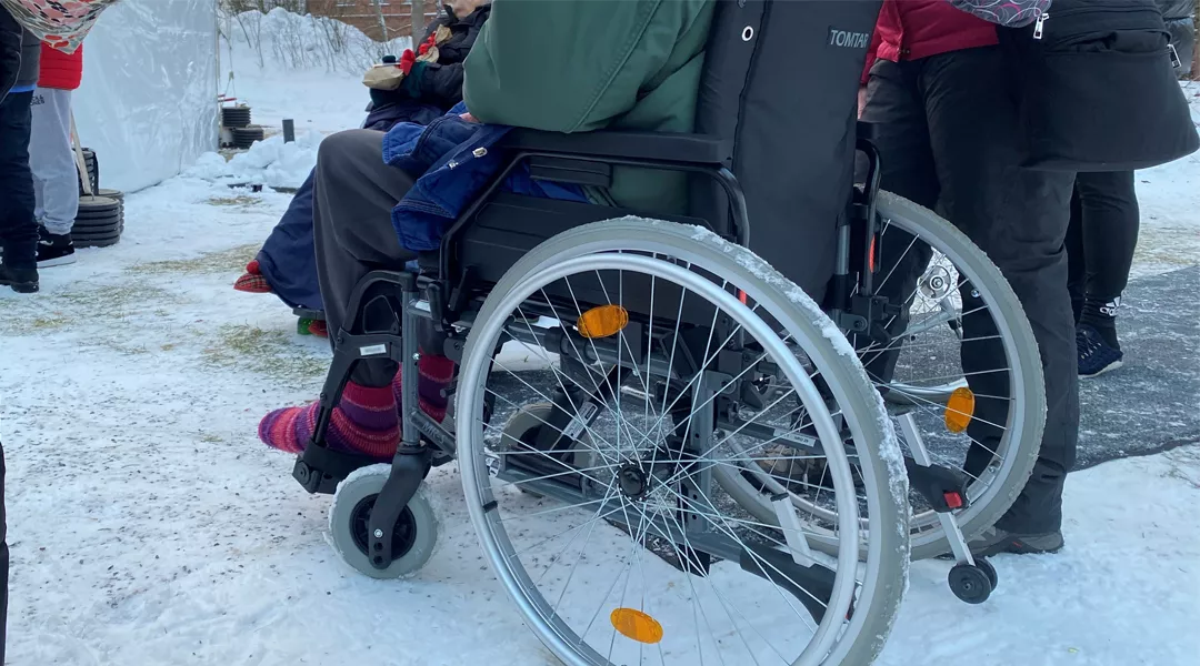 vanhus pyörätuolissa lumisella pihalla saattajan kanssa 