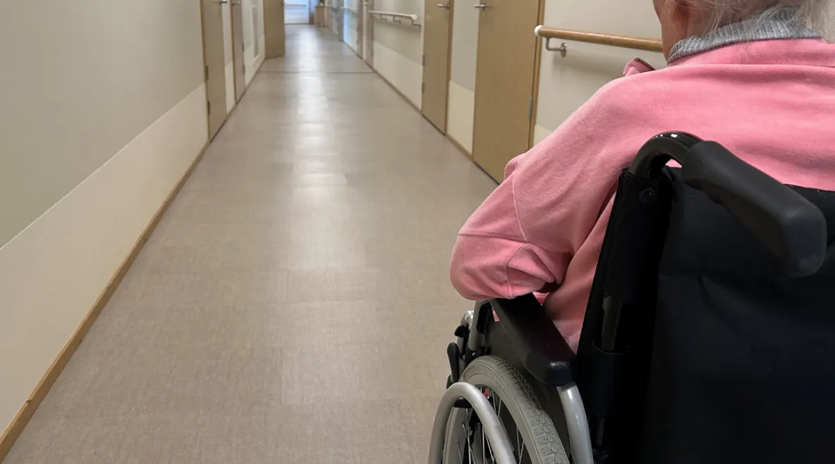 Vanhus sairaalan käytävällä pyörätuolissa. Puutteellinen kielitaito kuormittaa vanhusten hoidon työyhteisöjä ja vaarantaa potilasturvallisuutta.