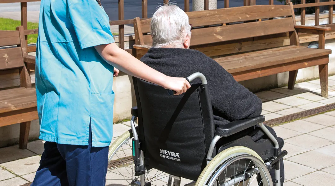 Hoitaja työntää vanhusta pyörätuolissa.