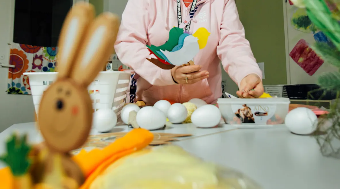 Päiväkodin työntekijä valmistelemassa lapsille askartelua pääsiäisteeman ympärillä. Pöydällä pupuhahmo ja kananmunia.