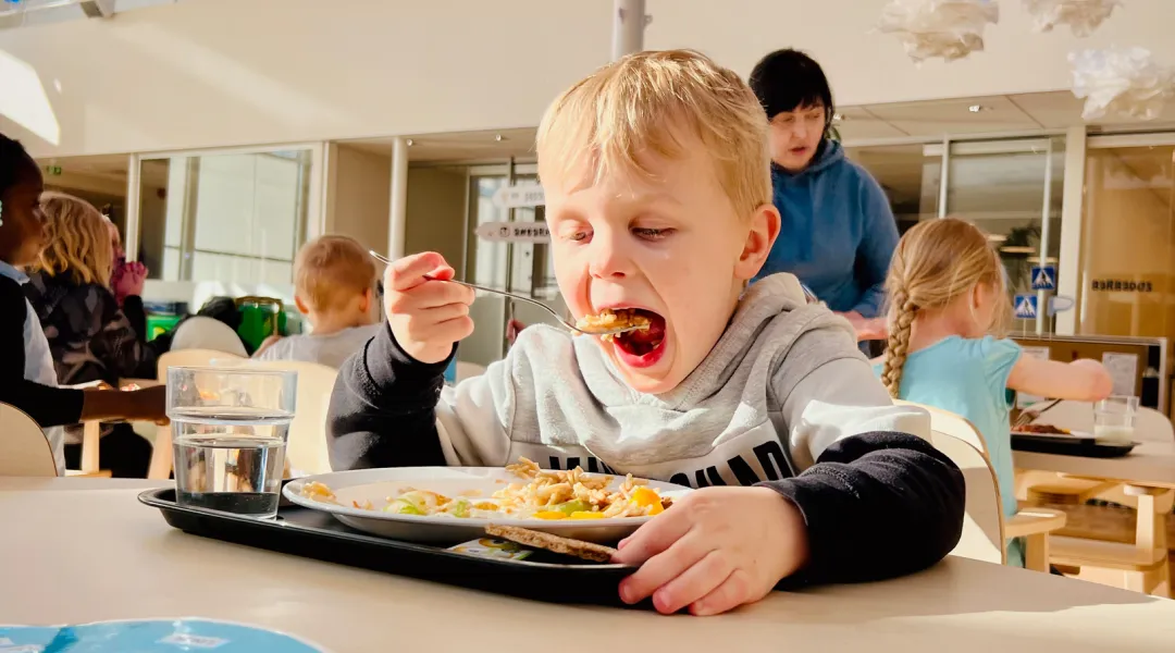 Pieni poika syö laittaa haarukallisen ruokaa suuhun päiväkodin lounaalla.