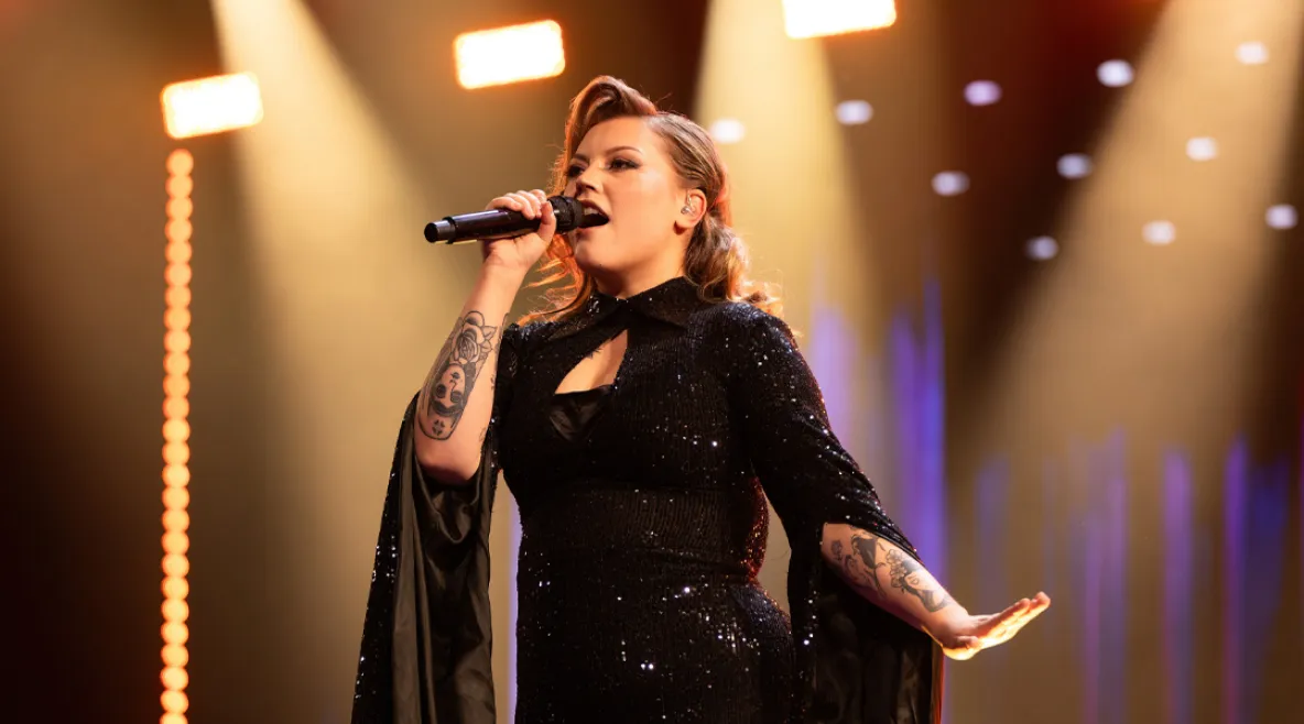 Tampereella työskentelevä sairaanhoitaja Justiina Luukaslammi on edennyt The Voice of Finlandissa semifinaalivaiheeseen. Justiina laulaa mikrofoniin tummassa dramaattisessa mekossa.