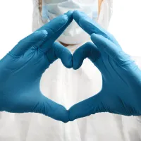 Kuvassa on henkilö valkoinen suojahaalari päällä, jonka sinisillä muovikäsineillä suojatut sormet muodostavat rinnan eteen sydämen. Kuva kuuluu Tehy-lehden blogitekstiin otsikolla: Ei voi olla totta, taas sinä olet töissä.