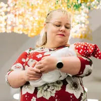 Kätilö Sari Räsänen pitää sylissään vauvaa, jolla on punainen tonttulakki.