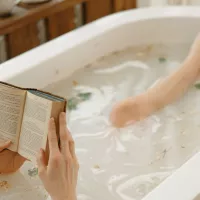 Kuvassa on nainen kylpyammeessa, joka lukee kirjaa.