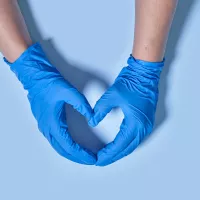 Kaksi sinisin suojakäsinein suojettua kättä muodostavat sormillaan sydämmen muodon. 