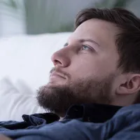 Kuvassa on mies, jolla on tummat hiukset ja parta. Hän tuijottaa vakavana ylöspäin.