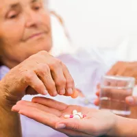 Kuvassa ikääntynyt naispotilas ottaa hoitajan kämmeneltä lääketabletteja