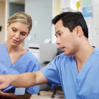 Kuvassa o mies- ja naissairaanhoitaja sinisissä suojatyöasuissa sairaalan kansliassa.