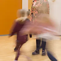 Lapset juoksevat aikuisen ympärillä.