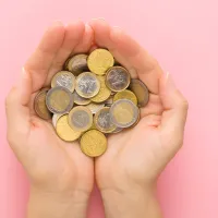 Nuoren aikuisen naisen kämmenet eurokolikoilla vaaleanpunaisella pöytätaustalla.