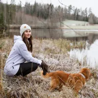 Kätilö Miia Sillman kuuraisessa talvimaisemassa vedenäärellä koiran kanssa.