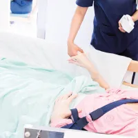 Hoitaja seisoo potilaan sängyn ääressä ja pitää tätä kädestä. 