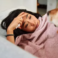 Nainen vuoteessa sairaana koiran seurassa. 