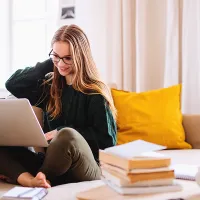 Kuvassa nuori nainen sohvalla tietokoneen kanssa
