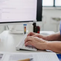 Hoitaja keskustelee potilaan kanssa. Taustalla tietokoneen näyttö.