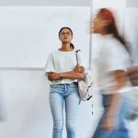 Nainen seisoo kiirehtävien ihmisten keskellä stressaantuneena kädet puuskassa ja katsoo ylöspäin.