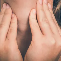 Nainen pitelee kaulaansa.