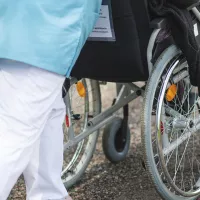 Anonyymi hoitaja työntää asiakasta pyörätuolissa.