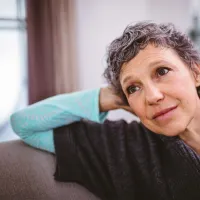 Hieman hiuksista harmaantunut nainen nojaa käteensä ja katsoo ikkunasta ulos.