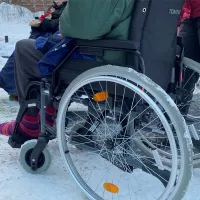vanhus pyörätuolissa lumisella pihalla saattajan kanssa 