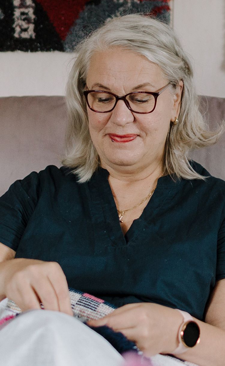 Marja-Liisa Haapakorva viimeistelee ryijyä olohuoneensa sohvalla.