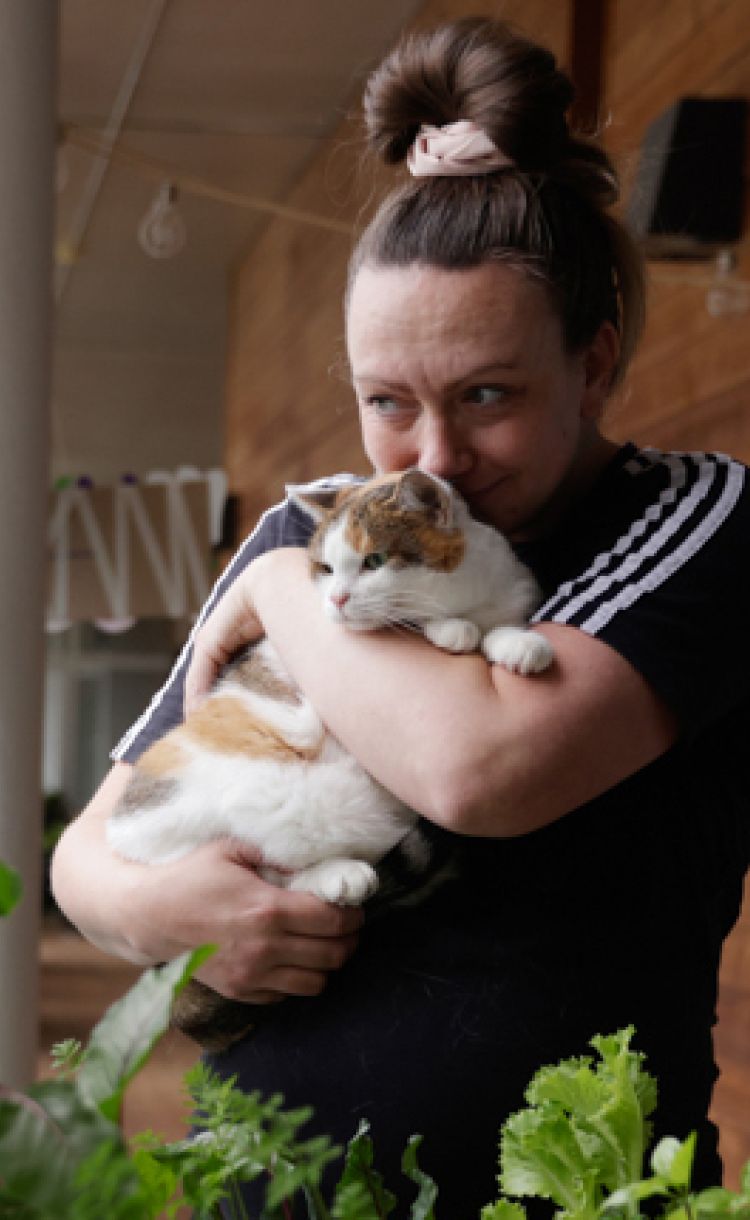 Lähihoitaja Kiia Malin Miiru-kissa sylissään Kontulan seniorikeskuksen parvekkeella.