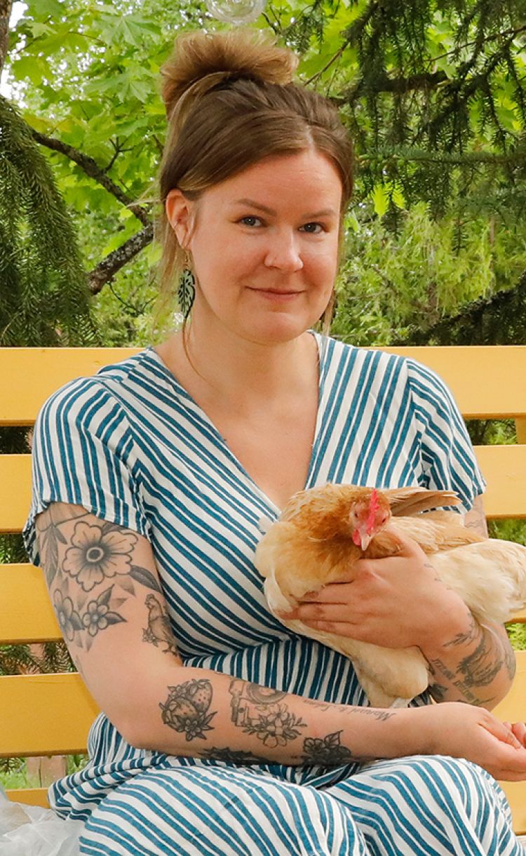 Julia Lehtilä istuu keltaisessa pihakeinussa kana sylissään.