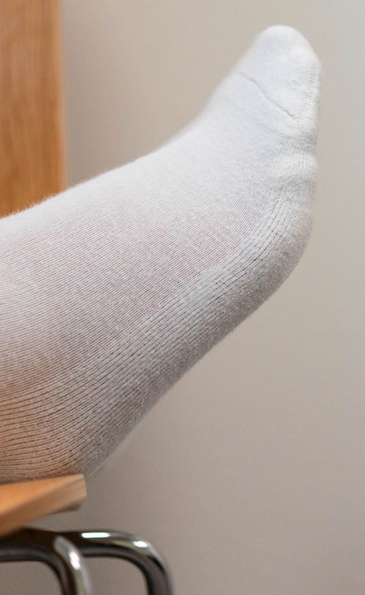 Jalka lepäämässä tuolin päällä. Näkyy vain hiukan lahjetta ja valkoinen sukka.