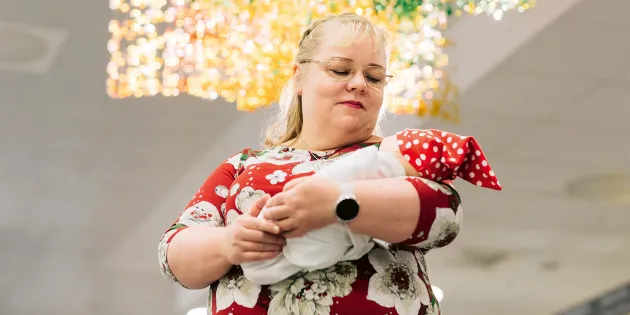 Kätilö Sari Räsänen pitää sylissään vauvaa, jolla on punainen tonttulakki.