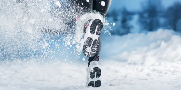 Lumessa juoksevan henkilön musta kengänpohja.