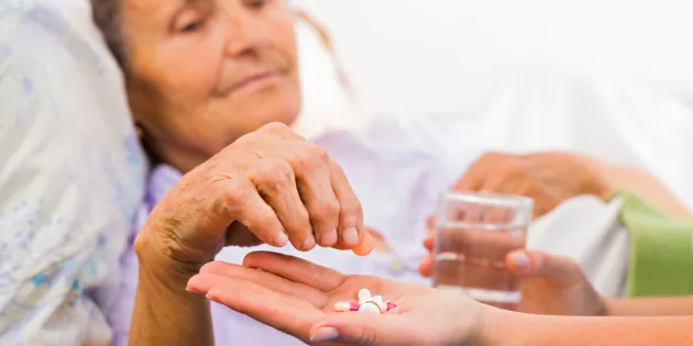 Kuvassa ikääntynyt naispotilas ottaa hoitajan kämmeneltä lääketabletteja