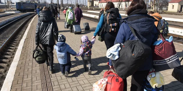 Ukrainalaisia pakolaisia rautatieasemalla raiteiden vieressä tavaroineen.