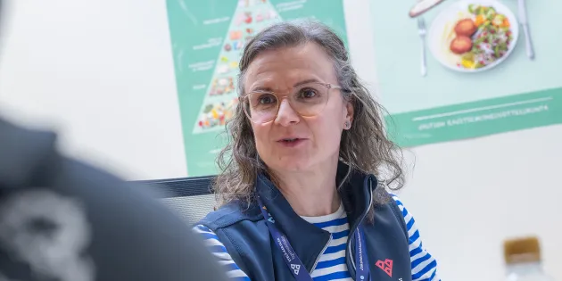 Hyvinvointivalmentaja Ulla Heimonen työhuoneessaan. Seinällä kuvia lautasmallista.
