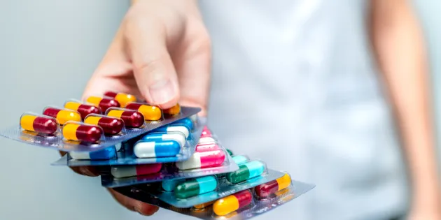 Apteekkihenkilökunta tai lääkäri pitelee kädessään antibioottikapselipillereitä ja antaa potilaalle tai lääkkeille