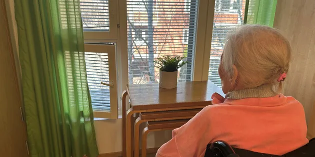 Vanhus istuu ja katselee ulos ikkunasta.