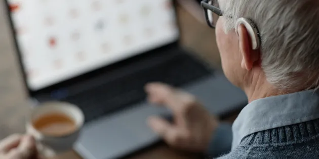 Tuoreen väitöstutkimuksen mukaan digipalvelujen onnistumista pitäisi mitata sillä, saako ihminen avun. Vanhus kuulokojeen kanssa käyttämässä tietokonetta.