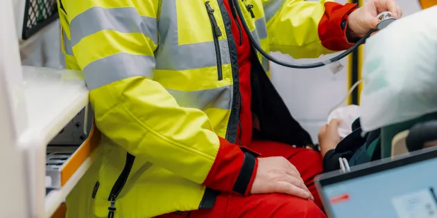 Hyvinvointialue päätti ensihoitajan työsuhteen perusteettomasti. Ensihoitaja kuuntelee potilaan hengitysääniä ambulanssissa.