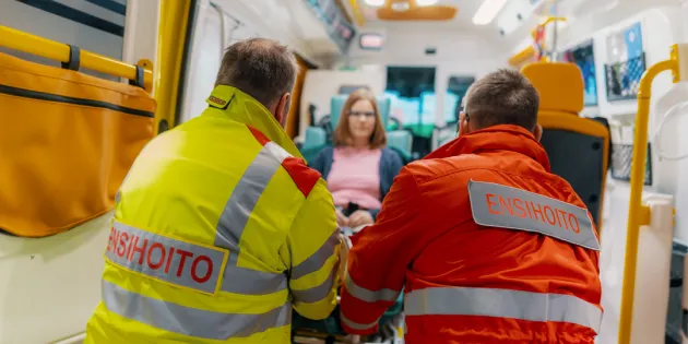 Kaksi ensihoitajaa auttavat potilaan ulos ambulanssista.
