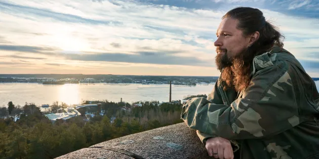 Mielenterveyshoitaja Vesa Suonsyrjä nojailee betoniseen kaiteeseen kaunis merimaisema taustalla.