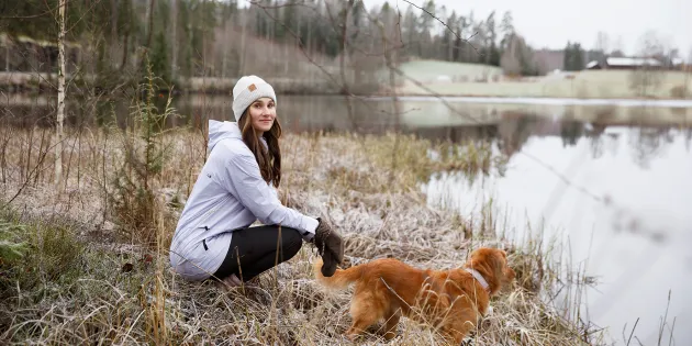 Kätilö Miia Sillman kuuraisessa talvimaisemassa vedenäärellä koiran kanssa.