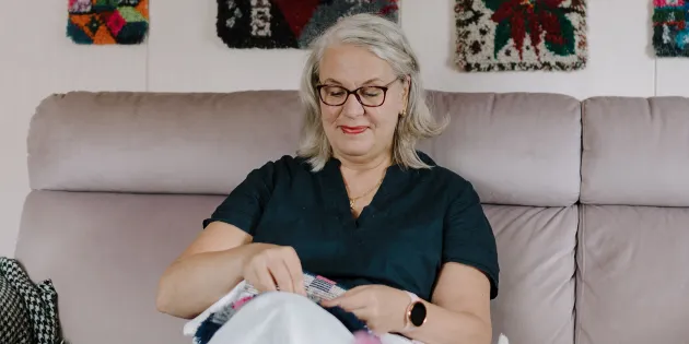 Marja-Liisa Haapakorva viimeistelee ryijyä olohuoneensa sohvalla.
