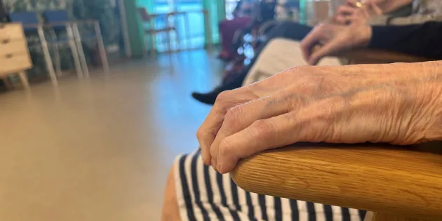 Vanhuksen käsi lepää tuolin käsinojalla hoivakodissa.