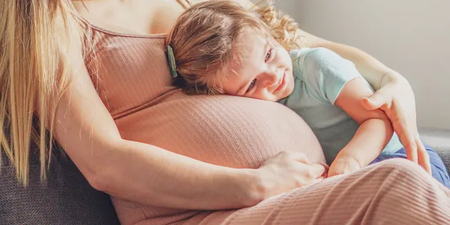 Raskaana oleva nainen, johon isompi lapsi nojaa.