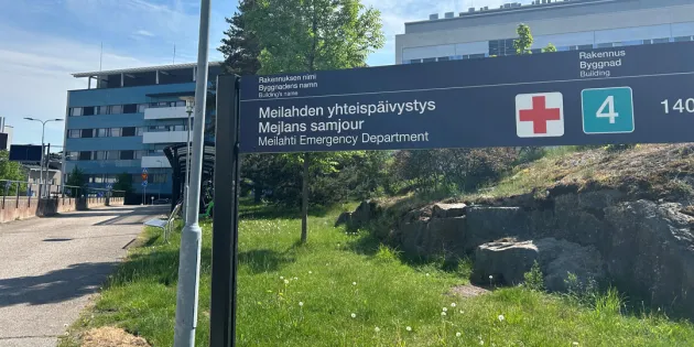 Meilahden sairaala-alue kesällä kuvattuna. Päivystys-kyltti nurmikolla. Hyvinvointialueiden säästöt ja rekrytointikiellot kiristävät sote-alan kesää. 